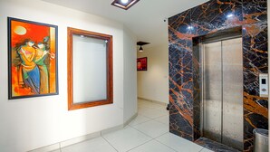 A hallway with a marble elevator, a framed painting, and a tiled floor. - Fabhotel Stevia (Dera Bassi)