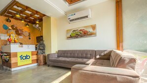 A hotel reception area with a wooden reception desk, a sofa, and a painting of cars on the wall. - Fabhotel Stevia (Dera Bassi)