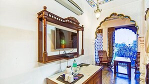Habitación de hotel con una televisión instalada en un marco de madera, una mesita con una bandeja de objetos y una silla.