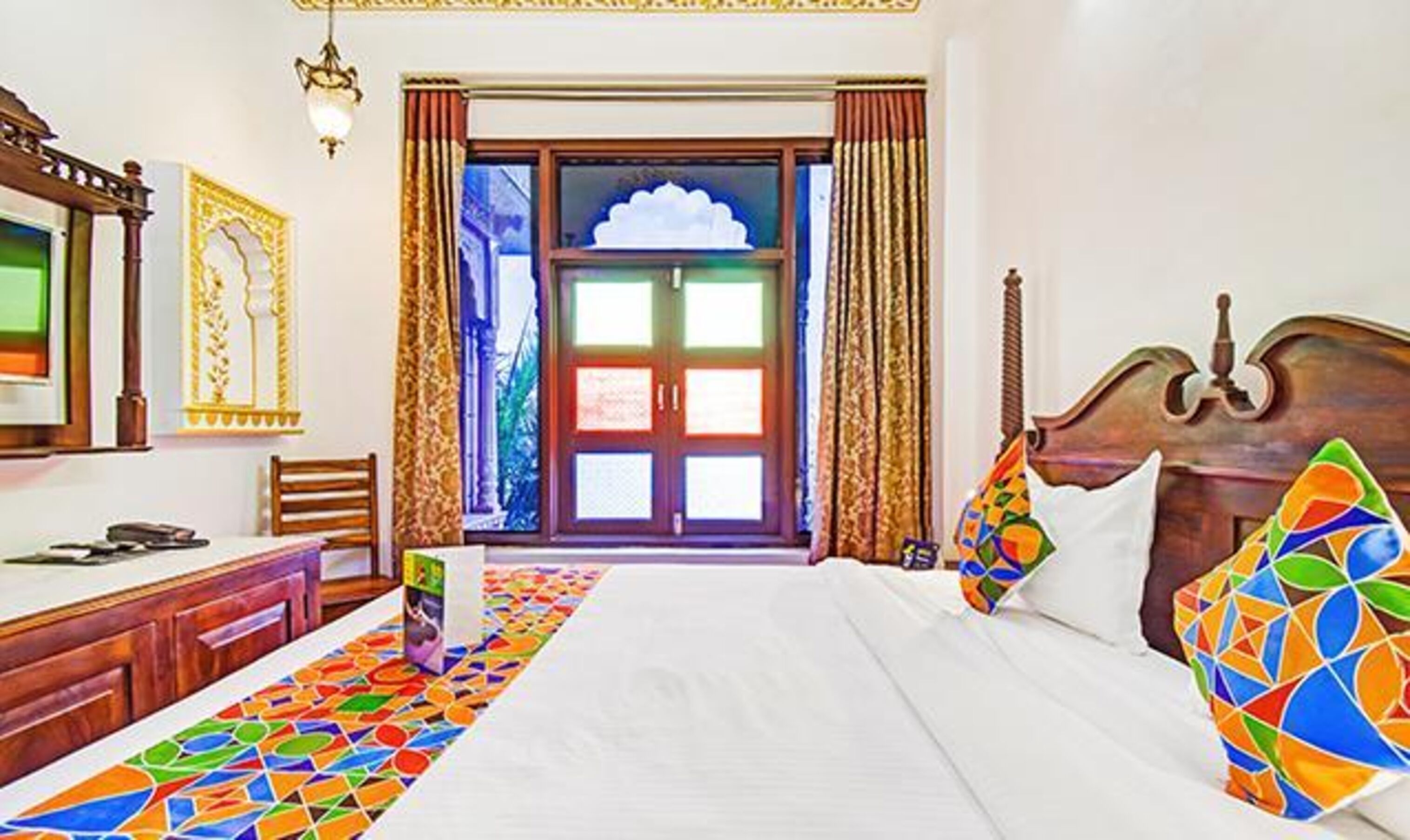Habitación de hotel con cama, escritorio, silla, ventana con cortinas y vistas al exterior.