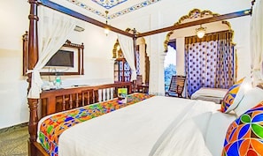 Un lit à baldaquin avec une couvre-lit aux couleurs vives, un téléviseur posé sur un meuble en bois et une fenêtre avec des rideaux.