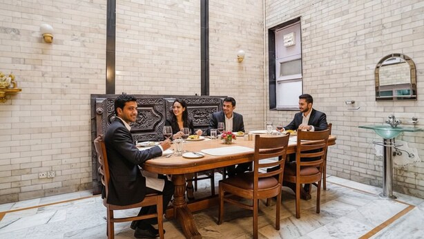 A dining area with a marble floor, a round wooden table, and a brick wall with a decorative panel. - FabHotel Goodwill Homes (New Delhi)