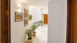 A hallway with a marble floor, wooden doors, and wall-mounted lights. - FabHotel Goodwill Homes (New Delhi)