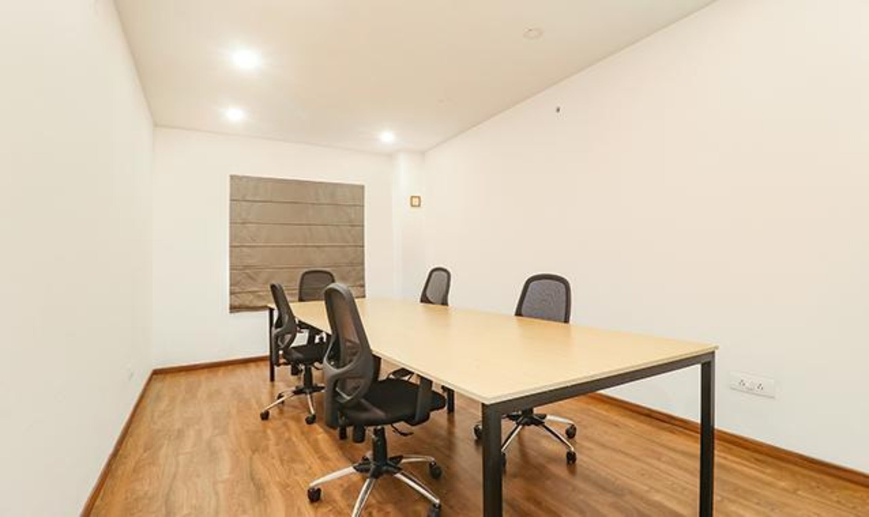 A conference room with a long table, four chairs, and a window with blinds.