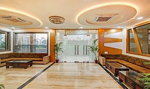 A spacious lobby with a marble floor, seating areas, and large windows offering views of buildings outside.