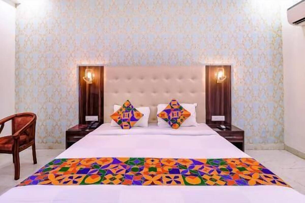 A hotel room with a bed, two nightstands, a chair, and patterned wallpaper.