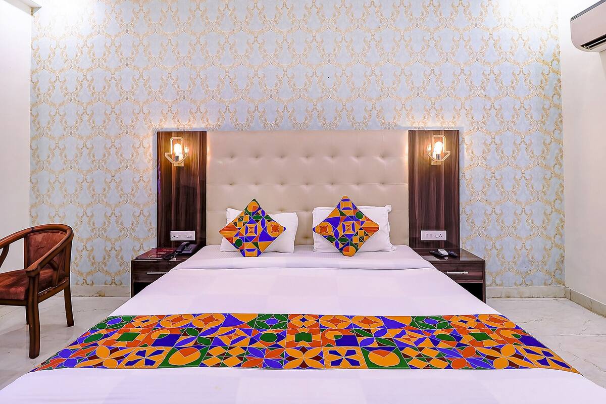 A hotel room with a large bed, two nightstands, a wooden chair, and patterned wallpaper.
