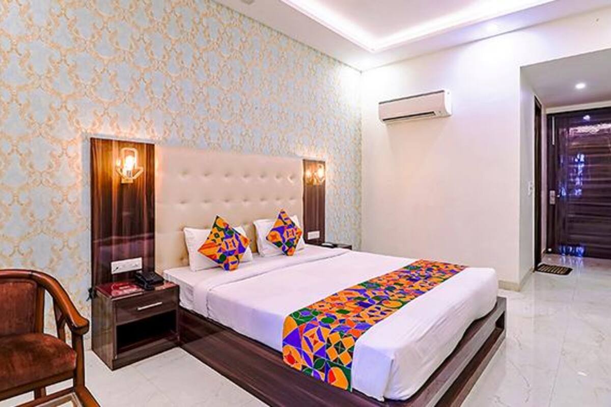 A hotel room with a large bed, a nightstand, a chair, a wall-mounted air conditioner, and a patterned wallpaper.