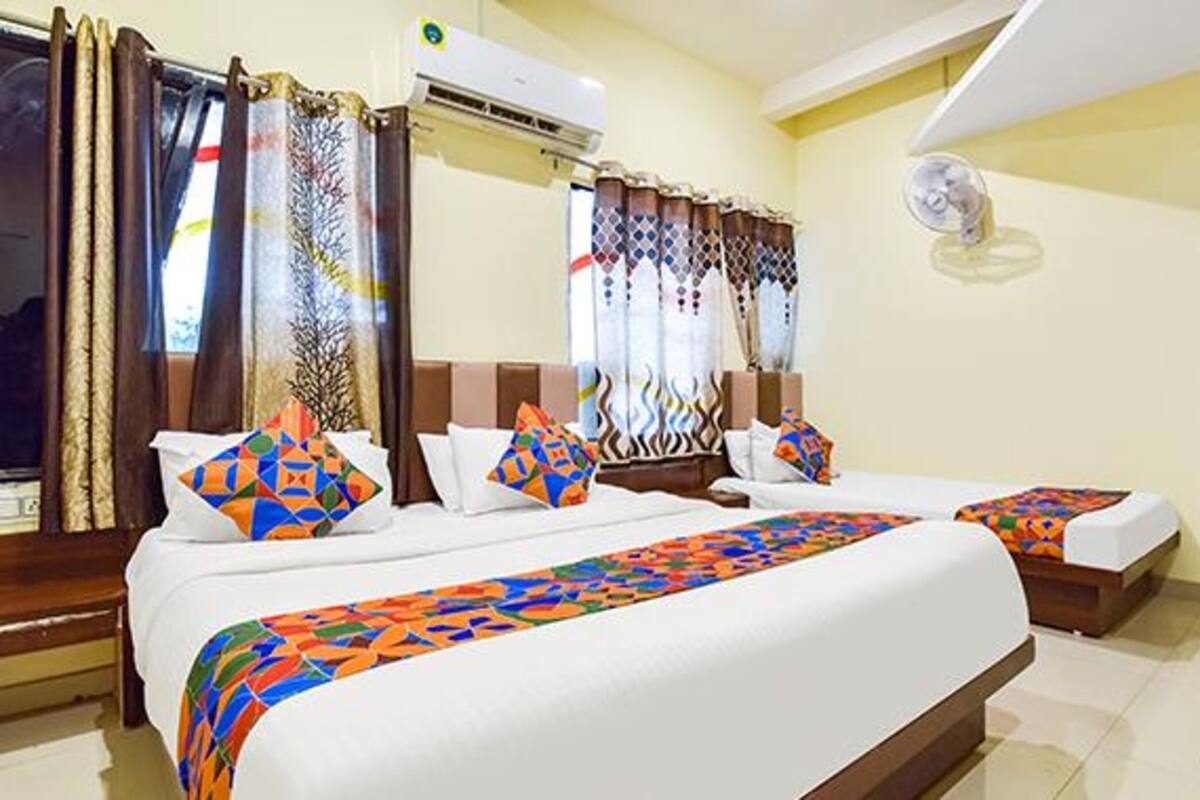 A hotel room with two beds, a large window with curtains, an air conditioning unit, and a ceiling fan.