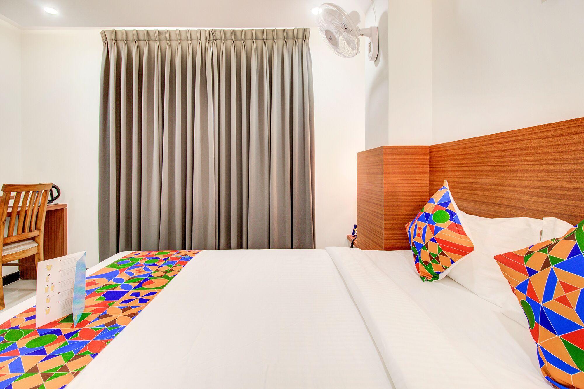 Habitación de hotel con cama, cabecera de madera, escritorio con silla y ventana con cortinas.