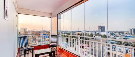 A balcony with a view of a cityscape, a small table, two chairs, and a rug.