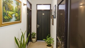 A hallway with a framed painting, a potted plant, and a door with a sign.