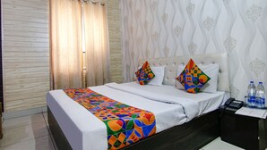 A hotel room with a bed, two pillows, a bedside table with a phone and water bottles, and a curtain.