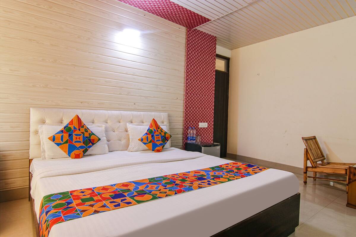 A neatly arranged bedroom with a large bed, two pillows, a wooden chair, and a red patterned wall.