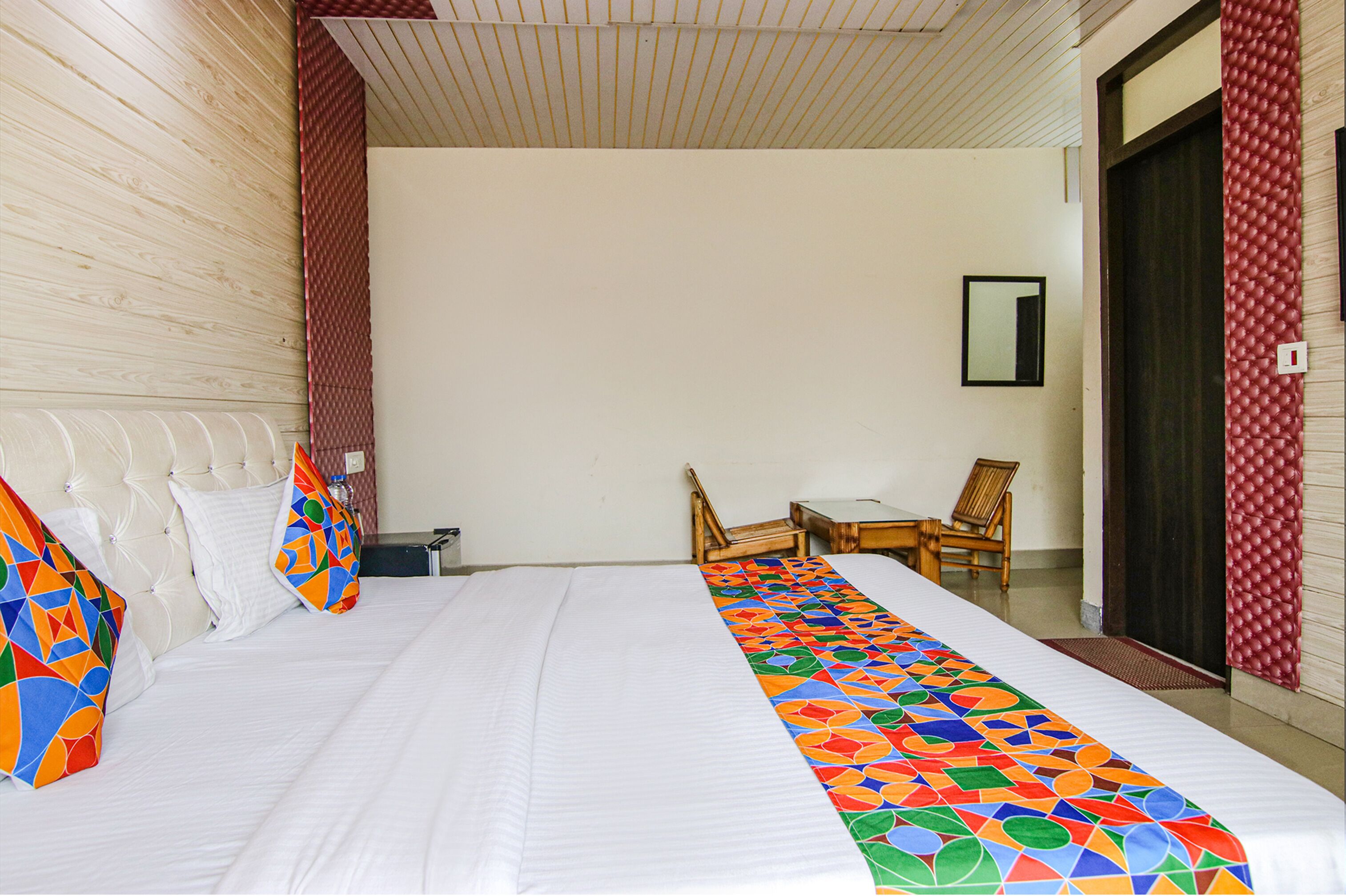 Une chambre d’hôtel avec un grand lit, deux chaises, une petite table et une porte avec un rideau rouge.