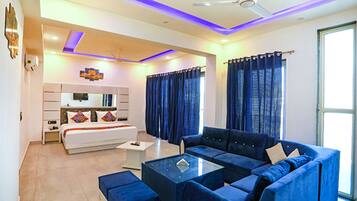 A modern hotel room with a large bed, a sofa, a coffee table, and a ceiling fan.