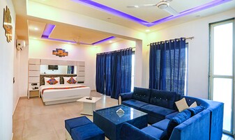A modern hotel room with a large bed, a sofa, a coffee table, and a ceiling fan.