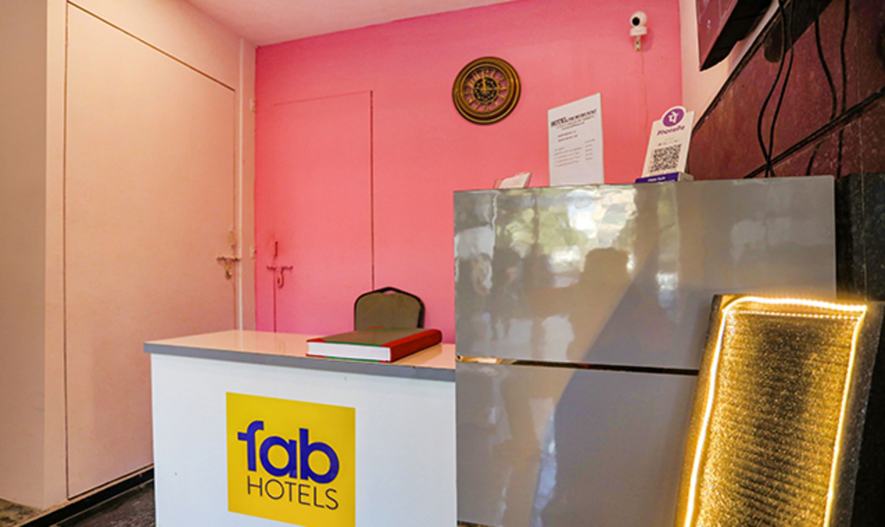 Een receptiebalie met een 'fab hotels' bord, een klok en een deur in een kamer met roze wanden.