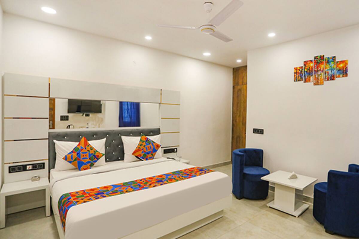 A modern hotel room with a large bed, a TV, a ceiling fan, and a small seating area with blue chairs.