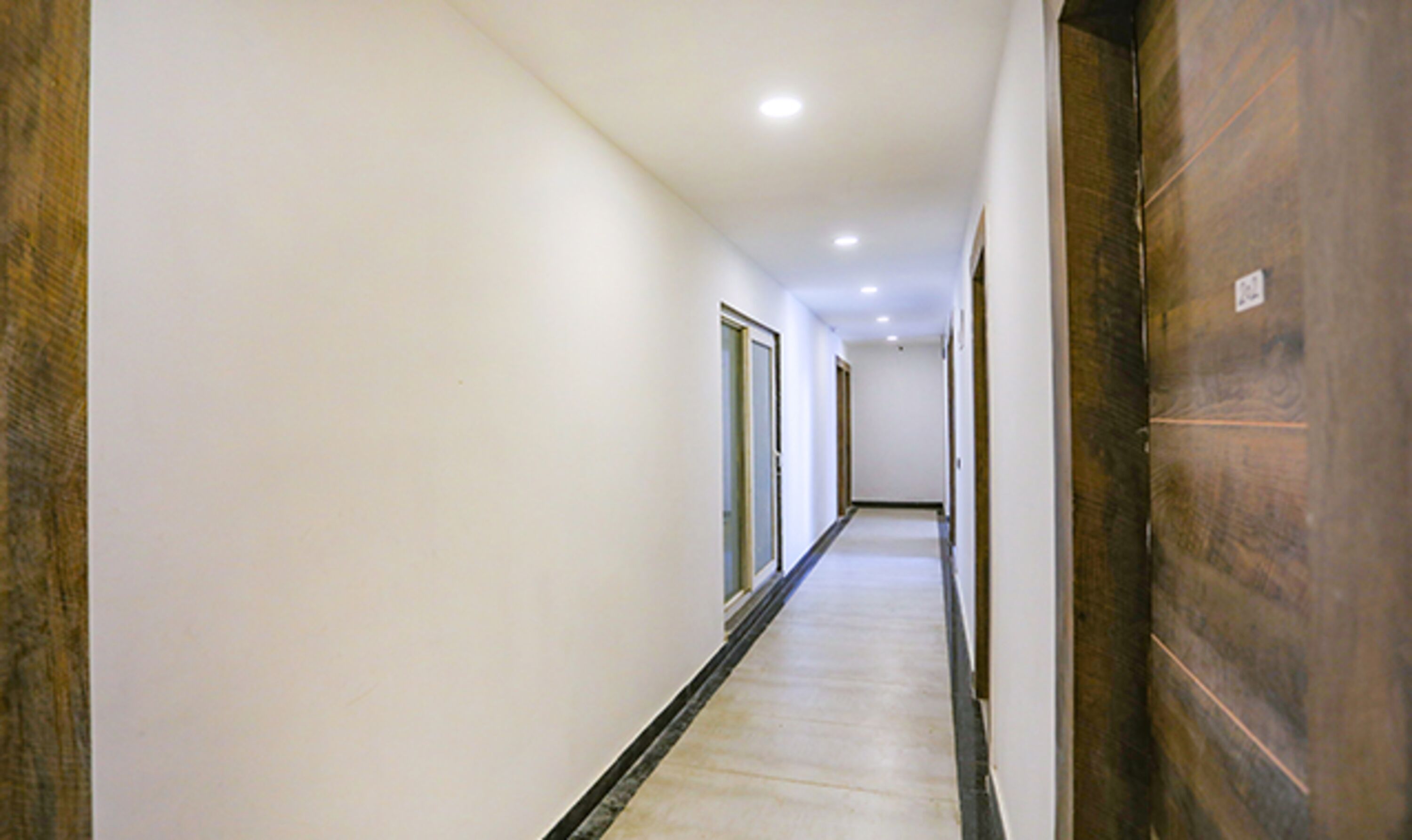 Un pasillo largo y estrecho con paredes blancas y una puerta de madera a la derecha.