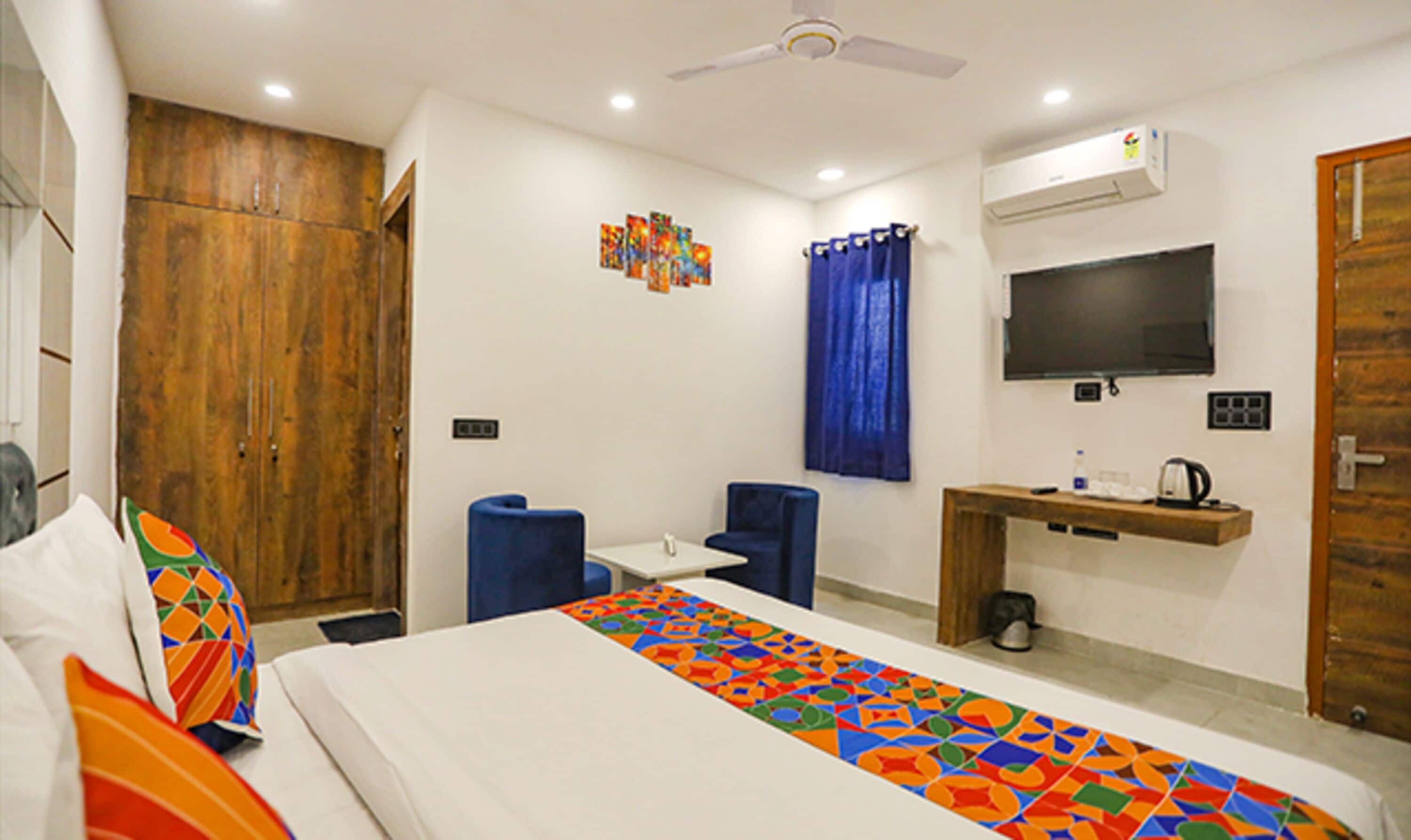 A hotel room with a bed, a desk with a chair, a television, and a wardrobe.