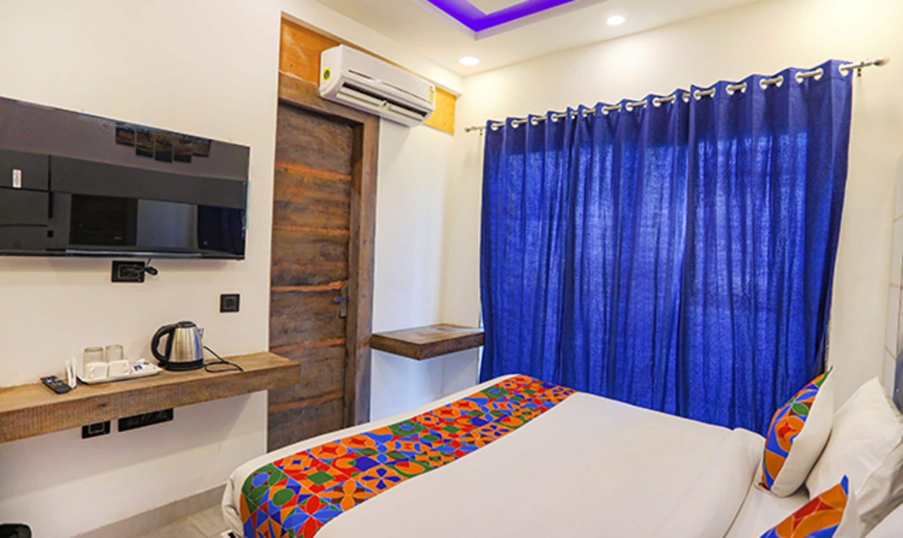 A hotel room with a bed, a TV mounted on the wall, a coffee maker, and a window with blue curtains.