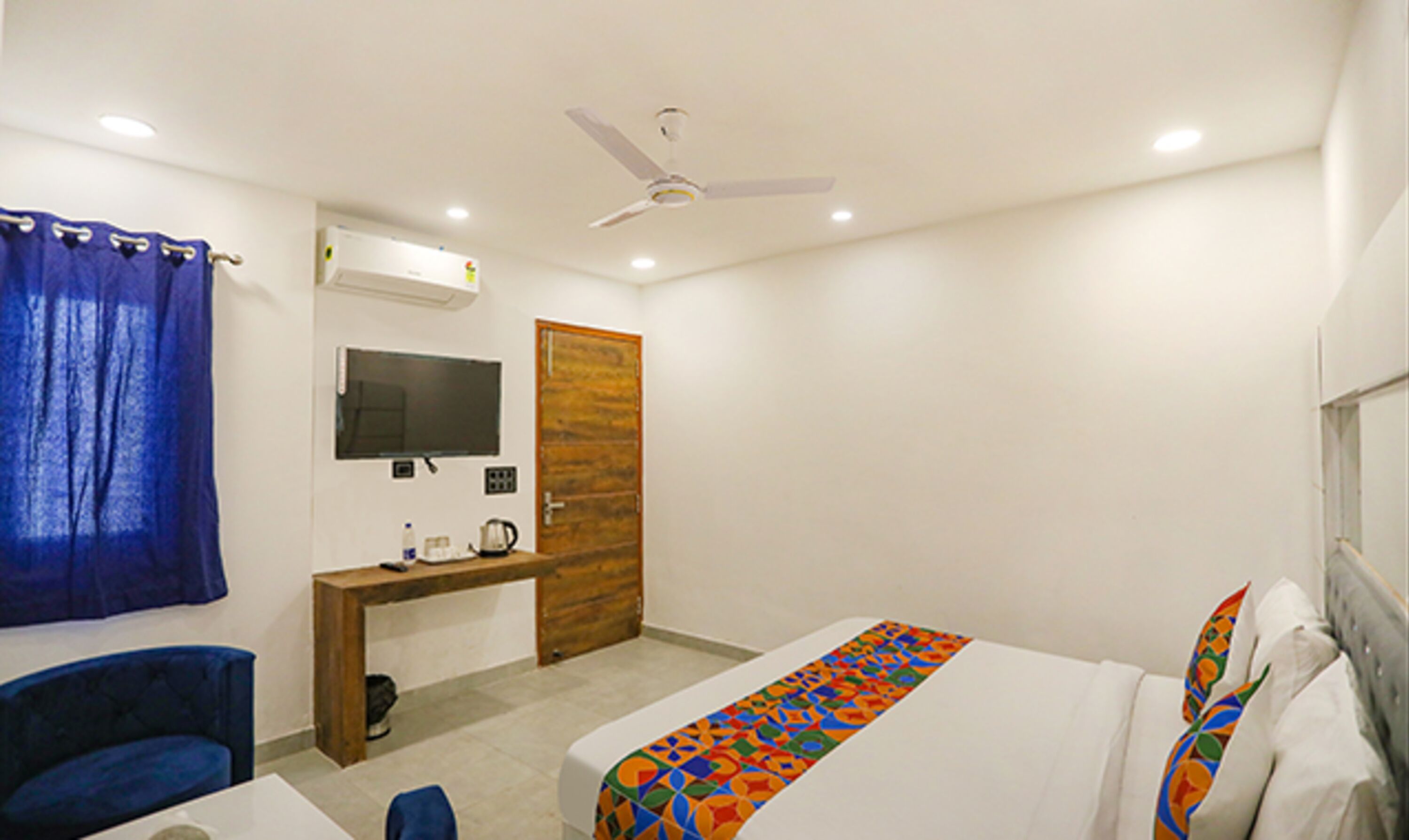 A hotel room with a bed, a desk, a chair, a television, and a ceiling fan.