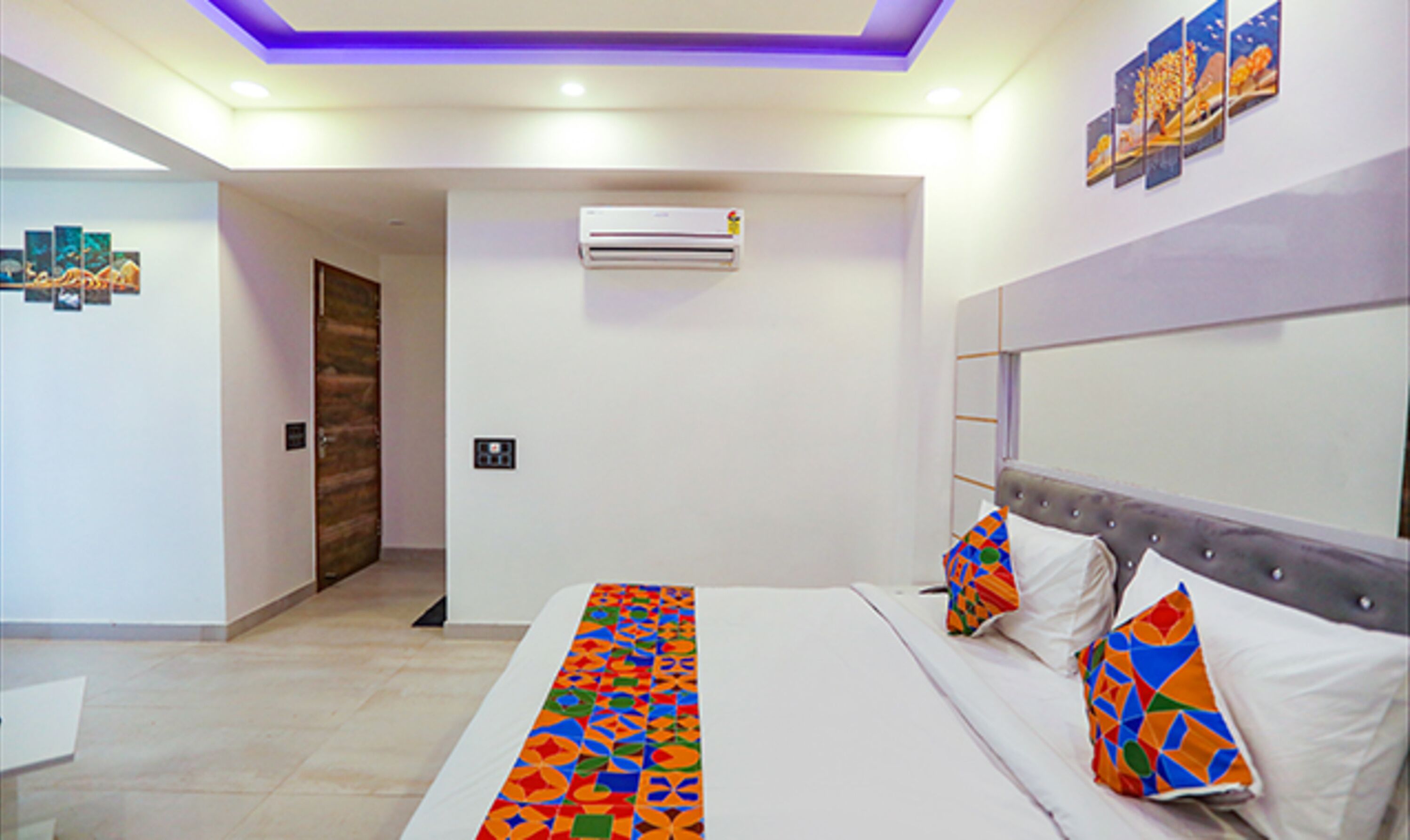 Een slaapkamer met een bed, kussens, een hoofdbord, een airconditioner en een deur.