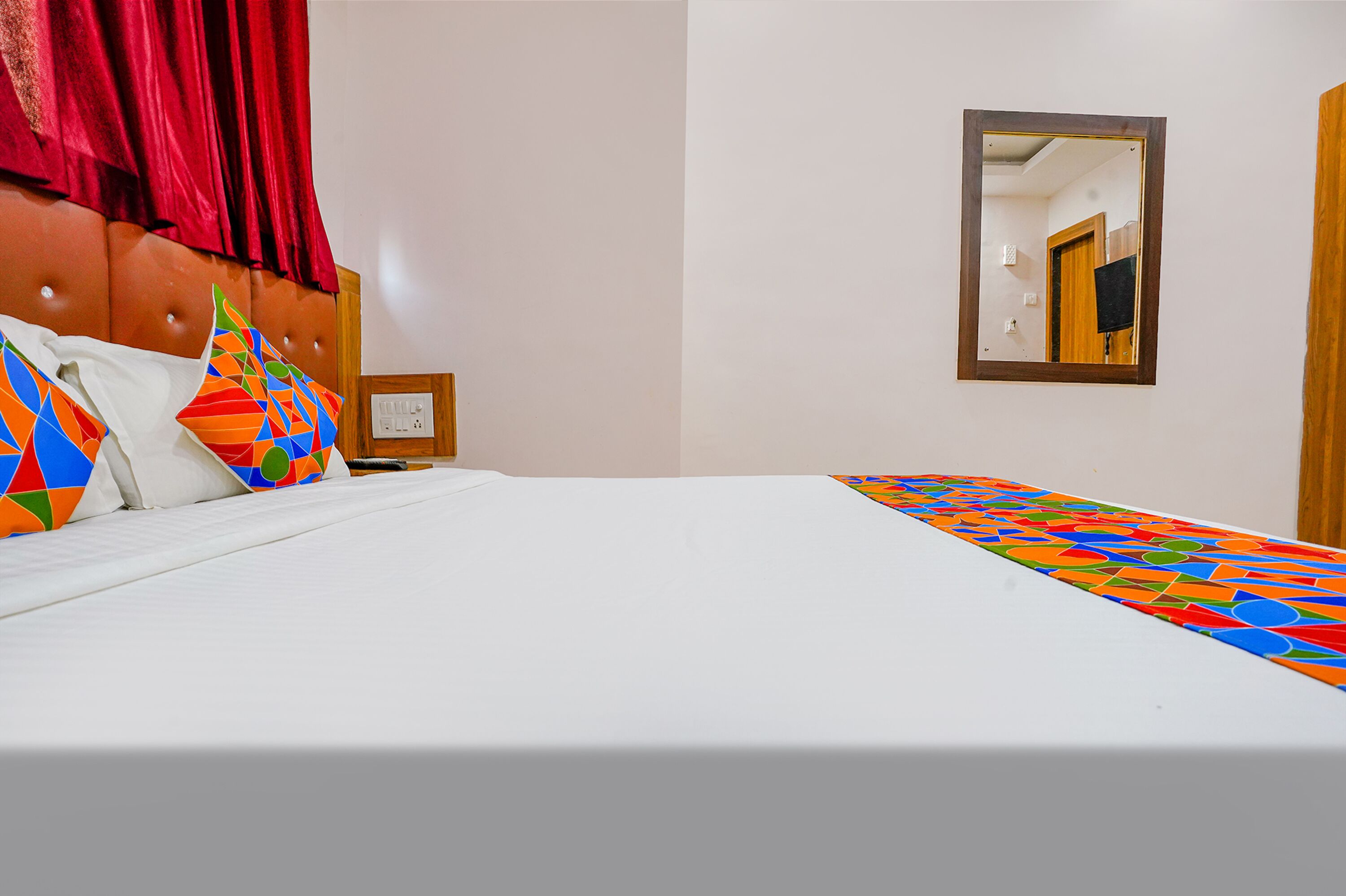 A hotel room with a bed, colorful pillows, a headboard, a mirror, and a wooden door.