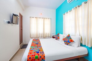 Una habitación de hotel con cama, cortinas, televisor y aire acondicionado instalado en la pared.