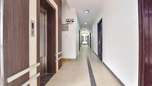 Un pasillo de hotel con puertas de madera, piso de baldosas claras y un largo corredor que lleva a una puerta al final.