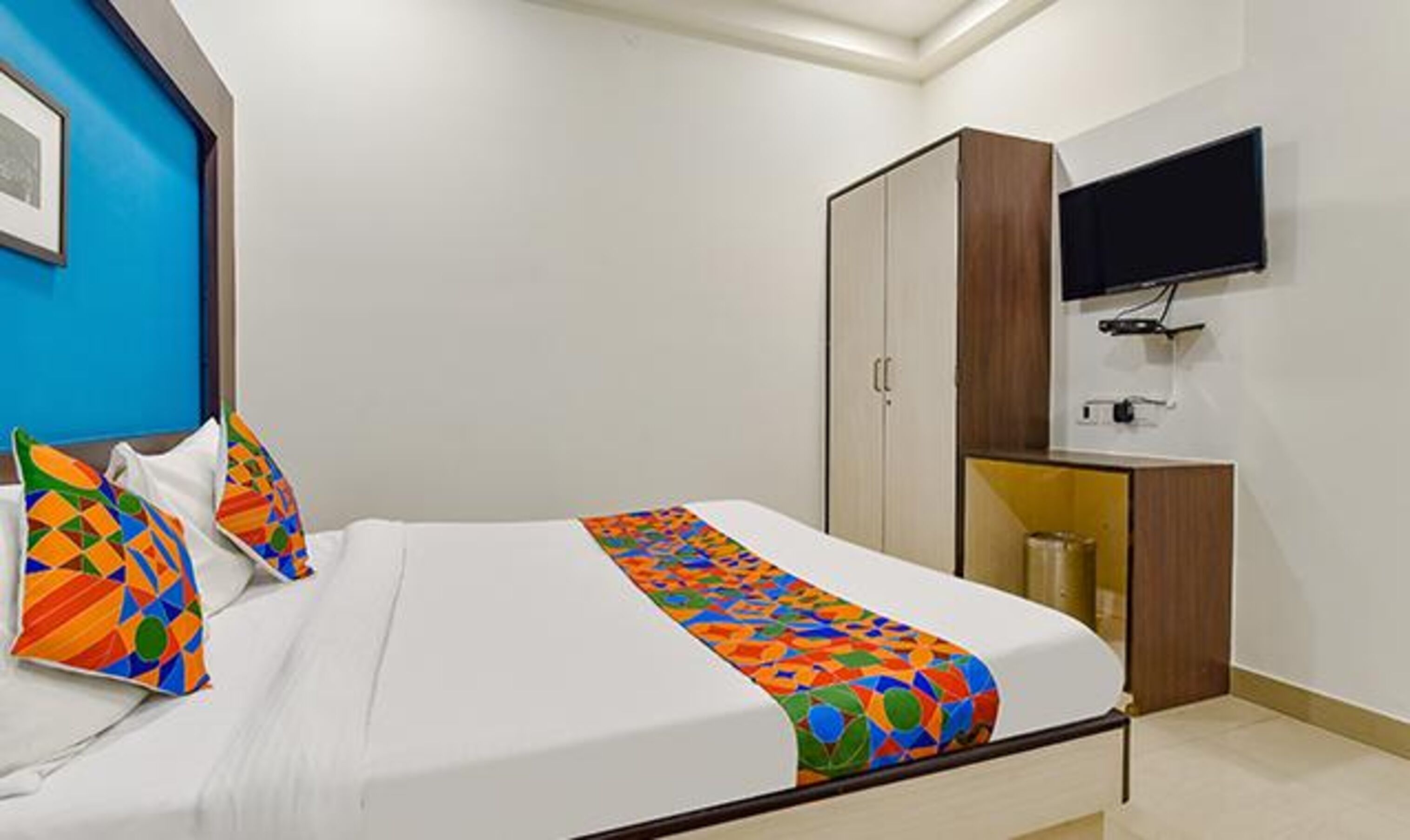 Una camera da letto con un letto, cuscini colorati, una TV a muro e un armadio.