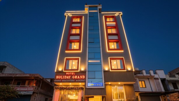 Um hotel com fachada moderna, apresentando uma entrada destacada com escadaria, e sinalização indicando ser o Holiday Grand.