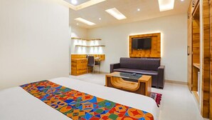 Quarto de hotel moderno com uma cama grande, um sofá, uma escrivaninha e uma televisão fixada na parede.