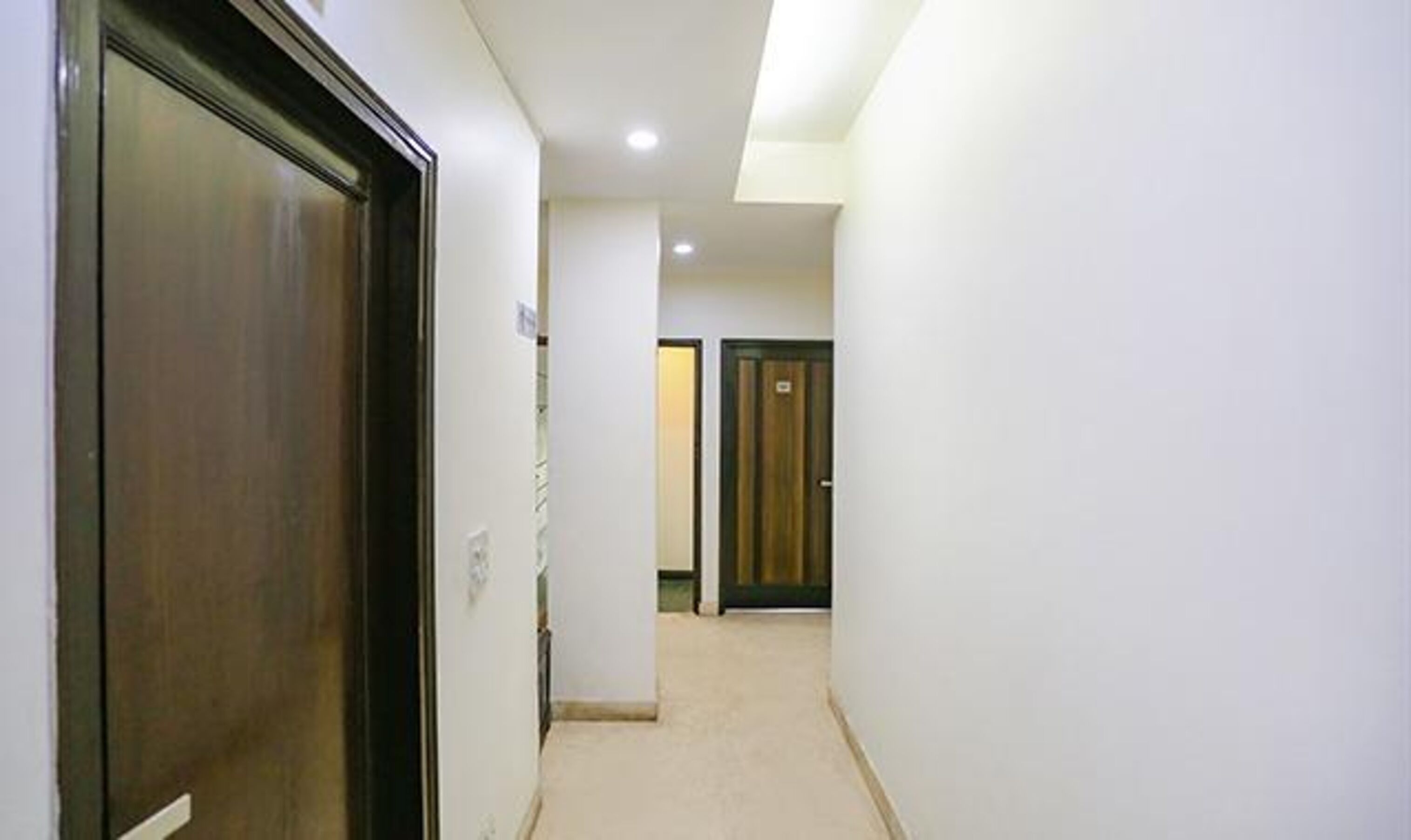 A narrow hallway with a wooden door on the left and a dark wooden door at the end.