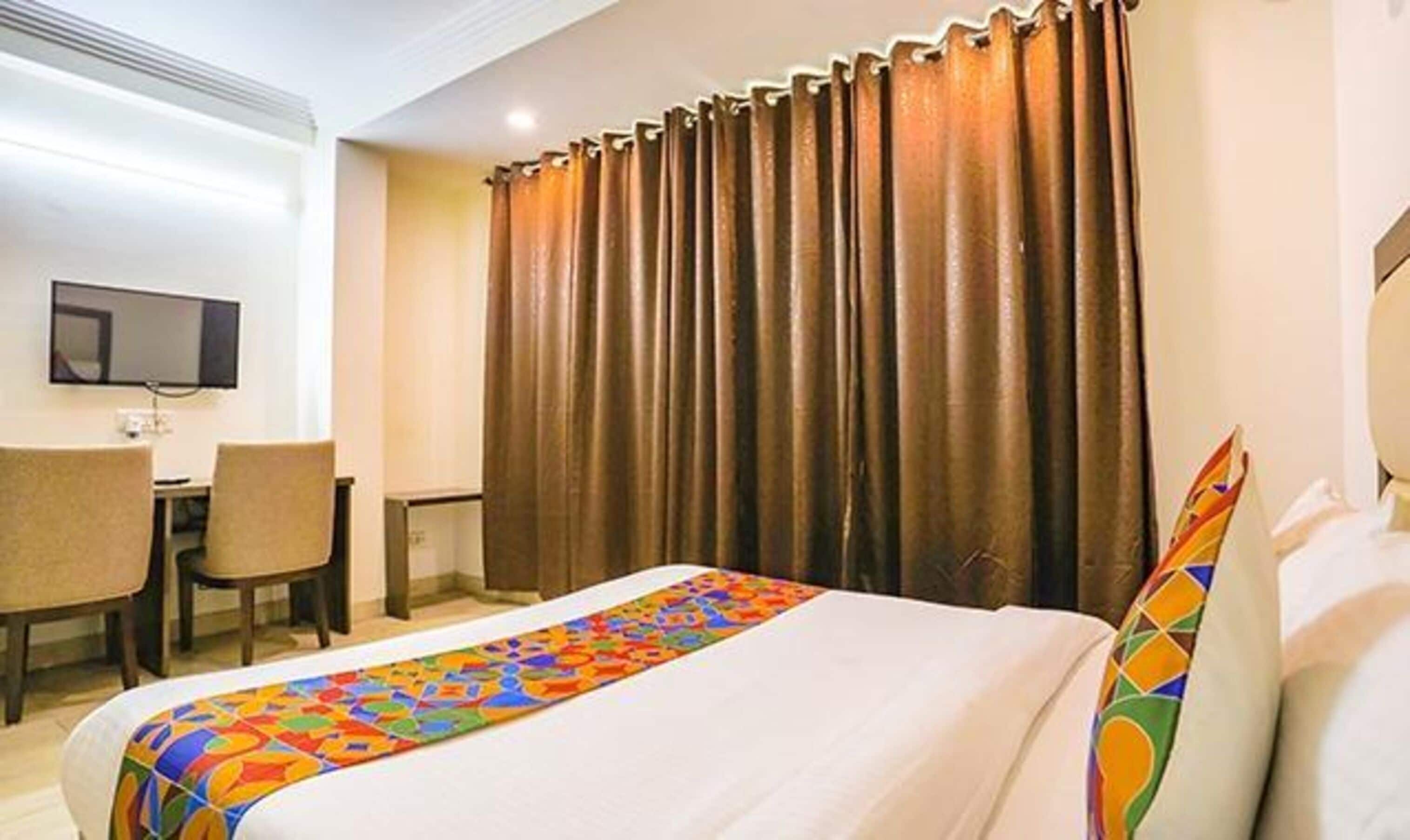 Quarto de hotel com uma cama, uma escrivaninha, uma cadeira e uma televisão na parede.