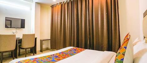 Quarto de hotel com uma cama, uma escrivaninha, uma cadeira e uma televisão na parede.