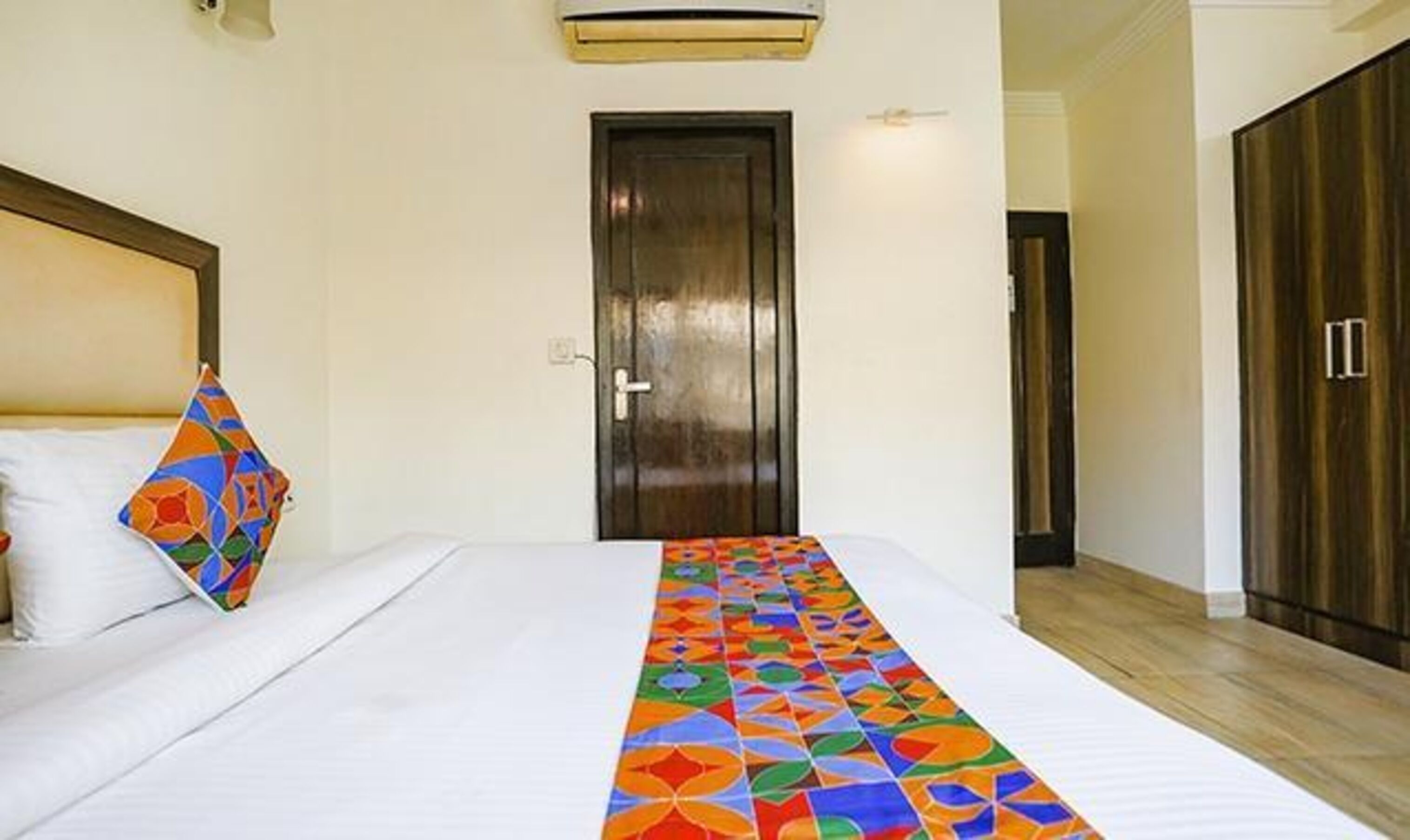 A hotel room with a bed, a wooden door, and a wardrobe.