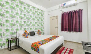 Een slaapkamer met een bed, nachtkastje, bureau, raam met gordijnen en een muur met een geometrisch patroon.