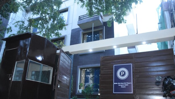 A modern building with a gated entrance, a sign indicating a parking area, and a motorcycle parked outside. - Fabhotel Posh Classic (Gurugram)