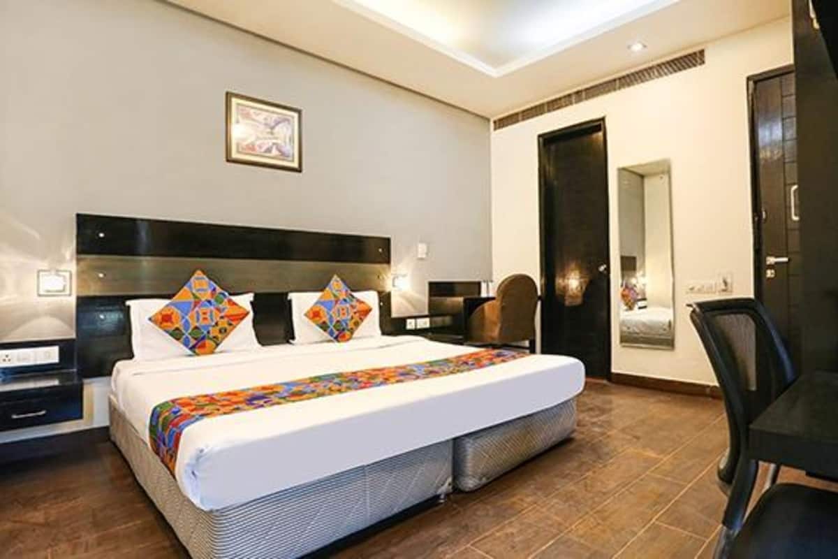 A hotel room with a large bed, a desk, a chair, and a mirror.