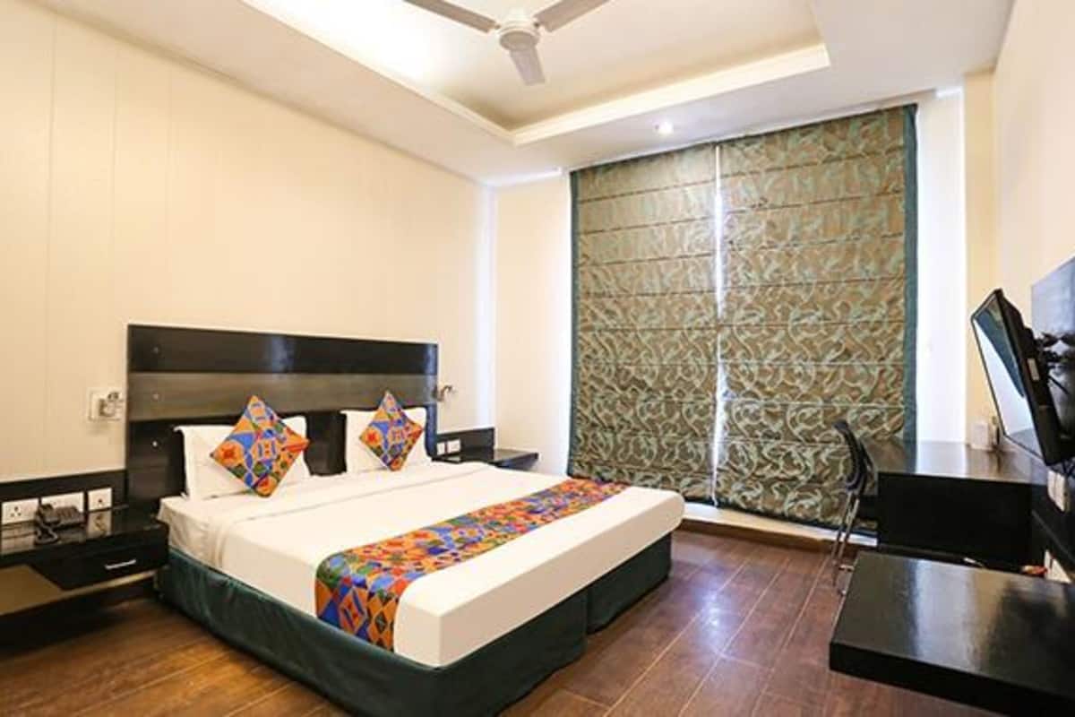 A hotel room with a bed, a desk, a television, and a window with patterned curtains.