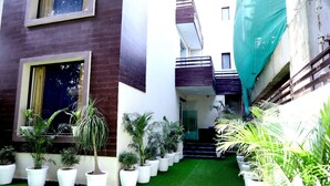 A narrow courtyard with artificial grass, potted plants, and a staircase leading to a balcony. - Fabhotel Posh Classic (Gurugram)