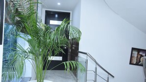 A staircase with a potted plant, a glass railing, and a door in the background. - Fabhotel Posh Classic (Gurugram)