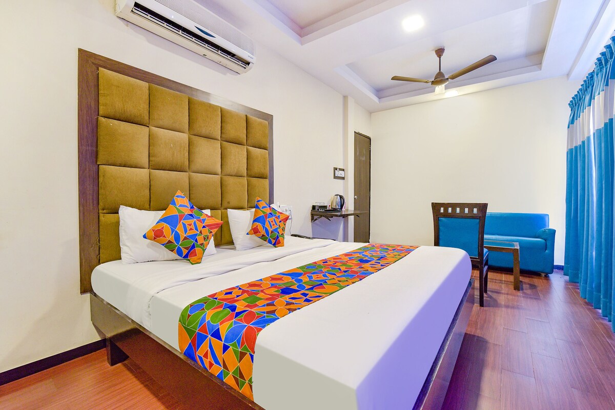 A hotel room with a large bed, a blue sofa, a ceiling fan, and an air conditioning unit.