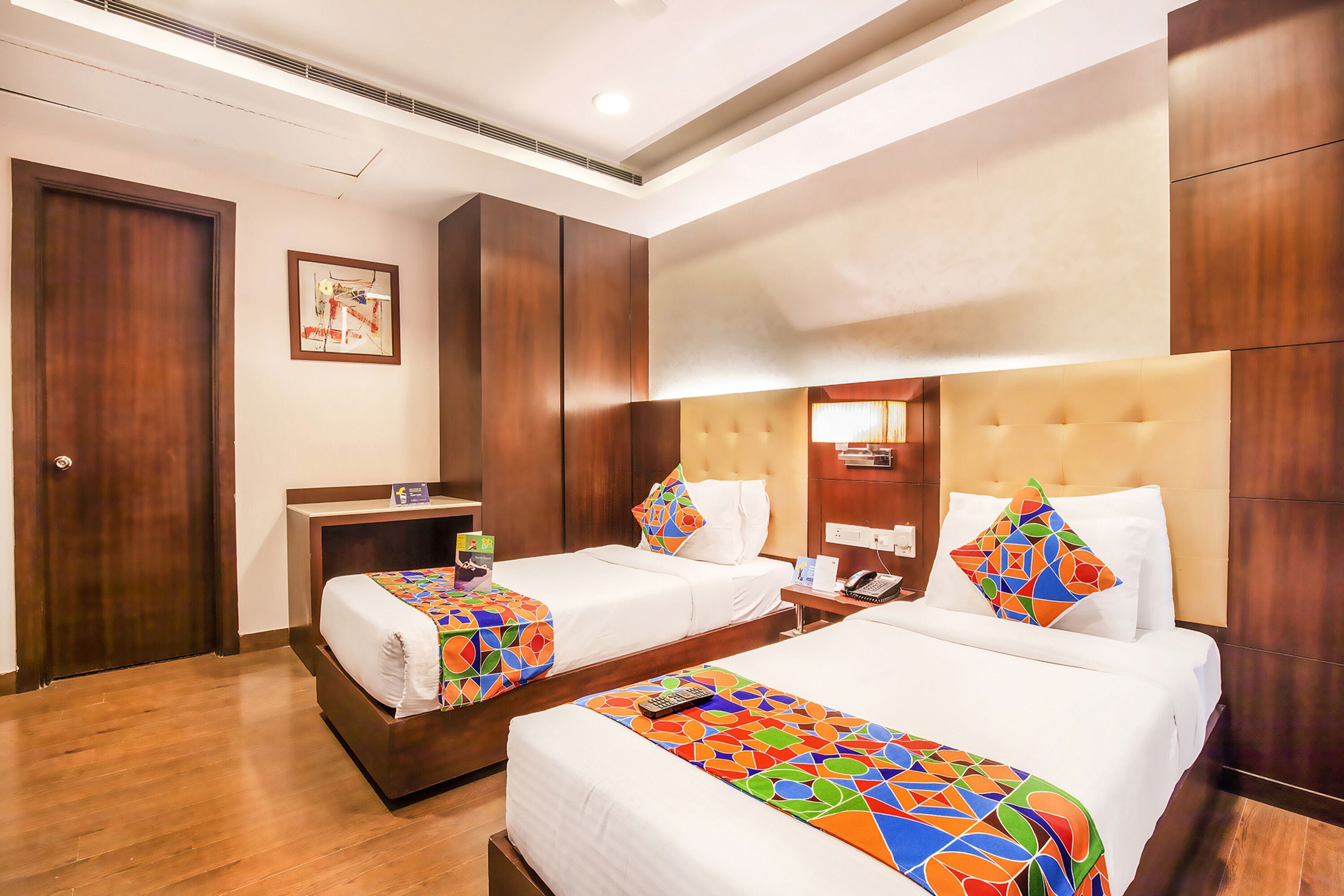 A hotel room with two beds, wooden flooring, a large mirror, and a painting on the wall.