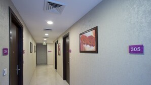 Corredor de hotel com portas numeradas 304 e 305, um quadro com uma flor na parede e sinal de saída.
