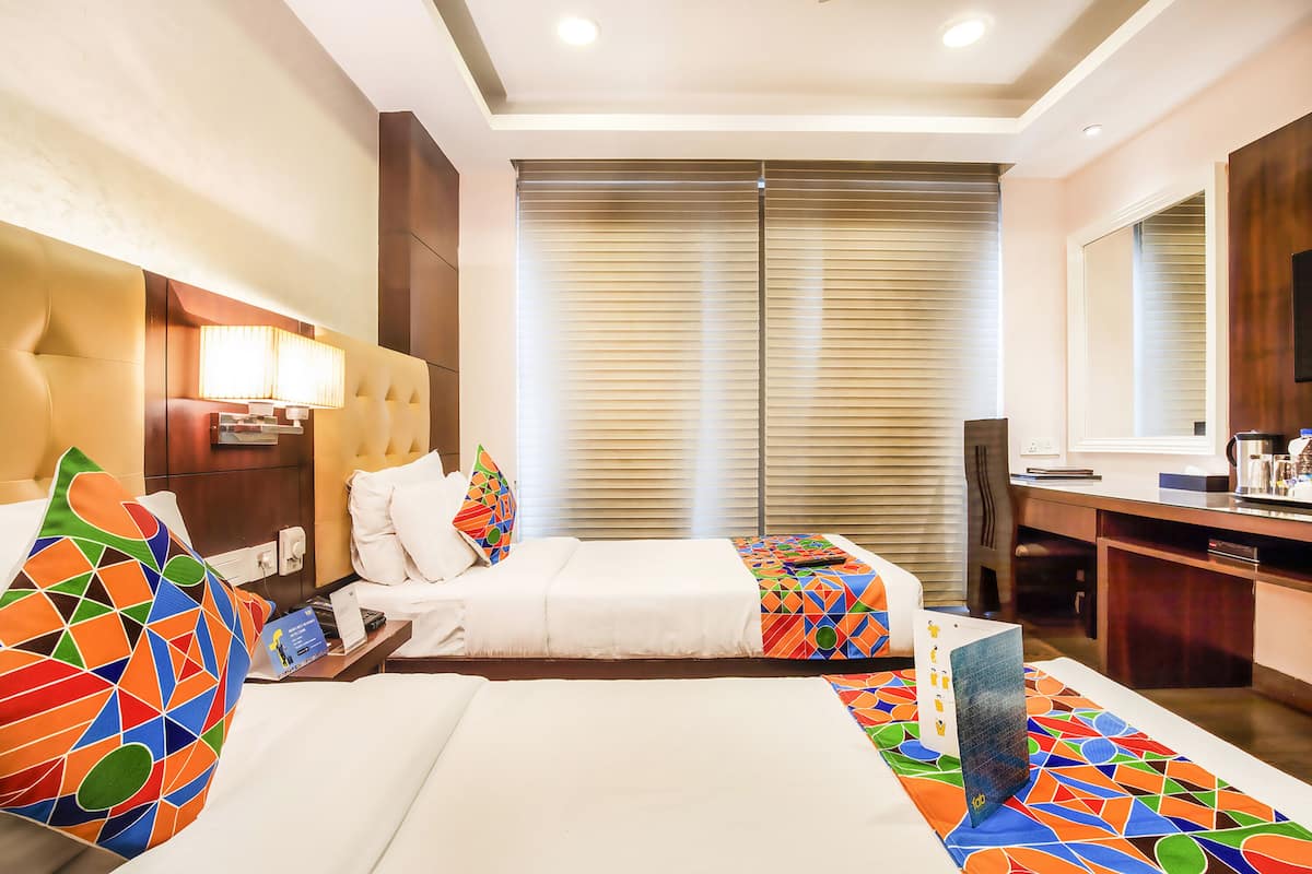 Habitación de hotel con dos camas, un escritorio, una silla, un televisor y un ventanal grande con persianas.