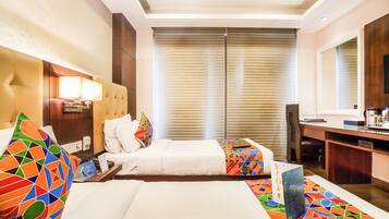 A hotel room with two beds, a desk, a chair, a TV, and a large window with blinds.