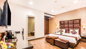 Quarto de hotel com uma cama grande, televisão, escrivaninha e uma cesta de lanches, além de uma janela com persianas.